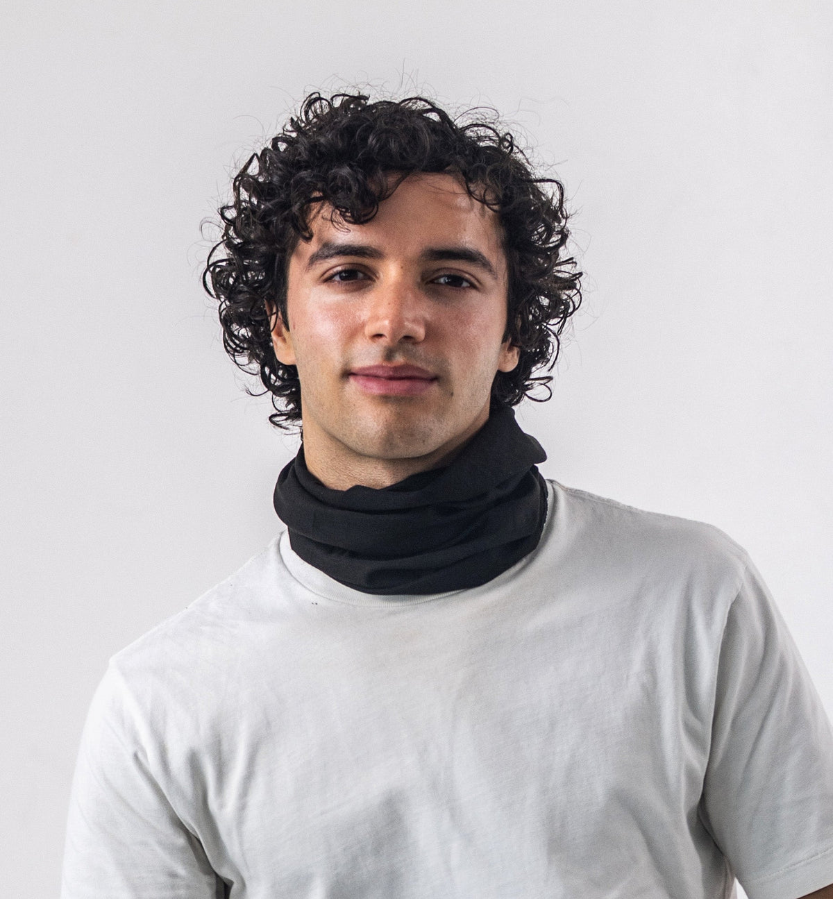 Man wearing a black Good Bands neck gaiter bunched at the collar over a cream tee on a light gray background