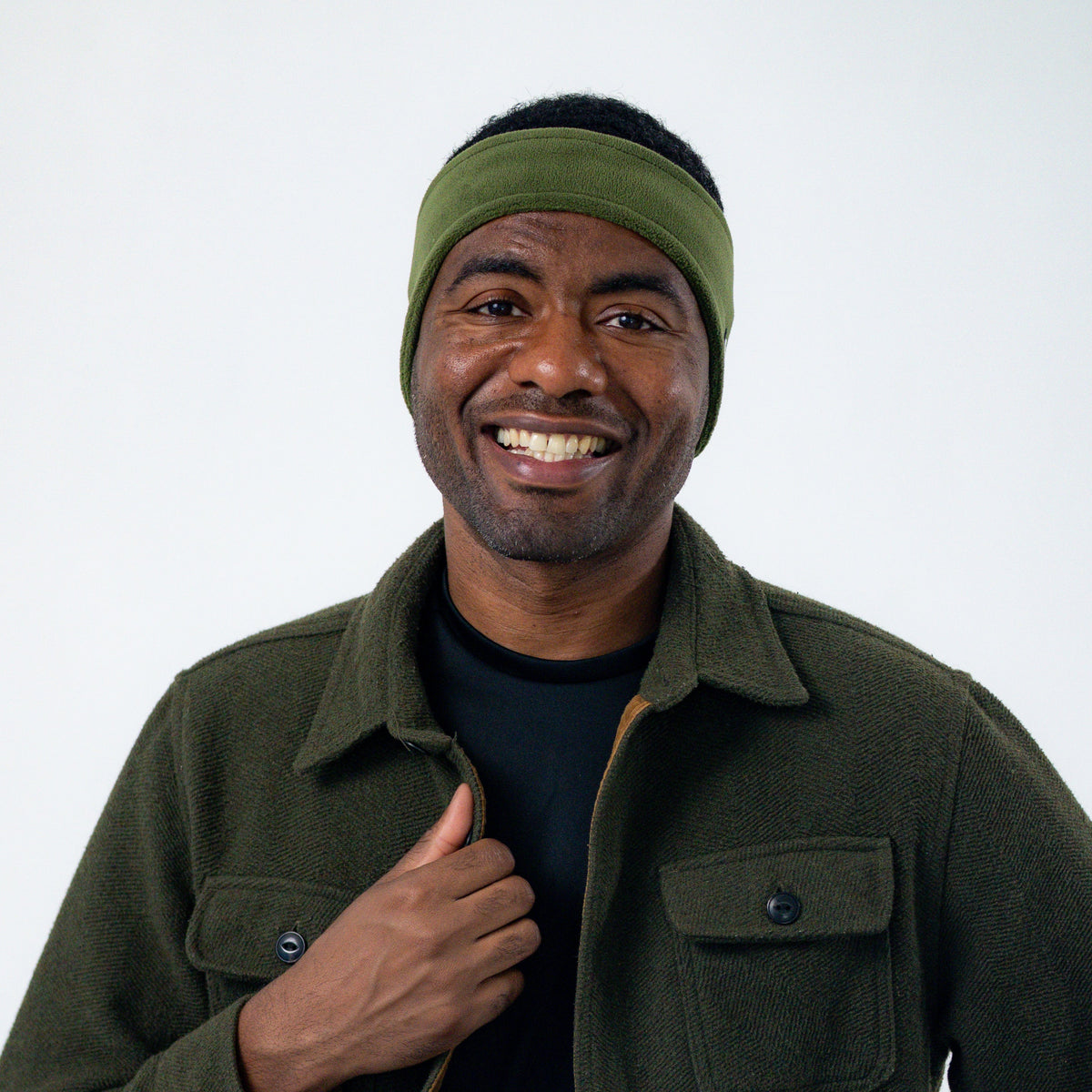 Smiling man wearing an olive green Good Bands winter ear warmer and a fleece jacket against a light gray studio background