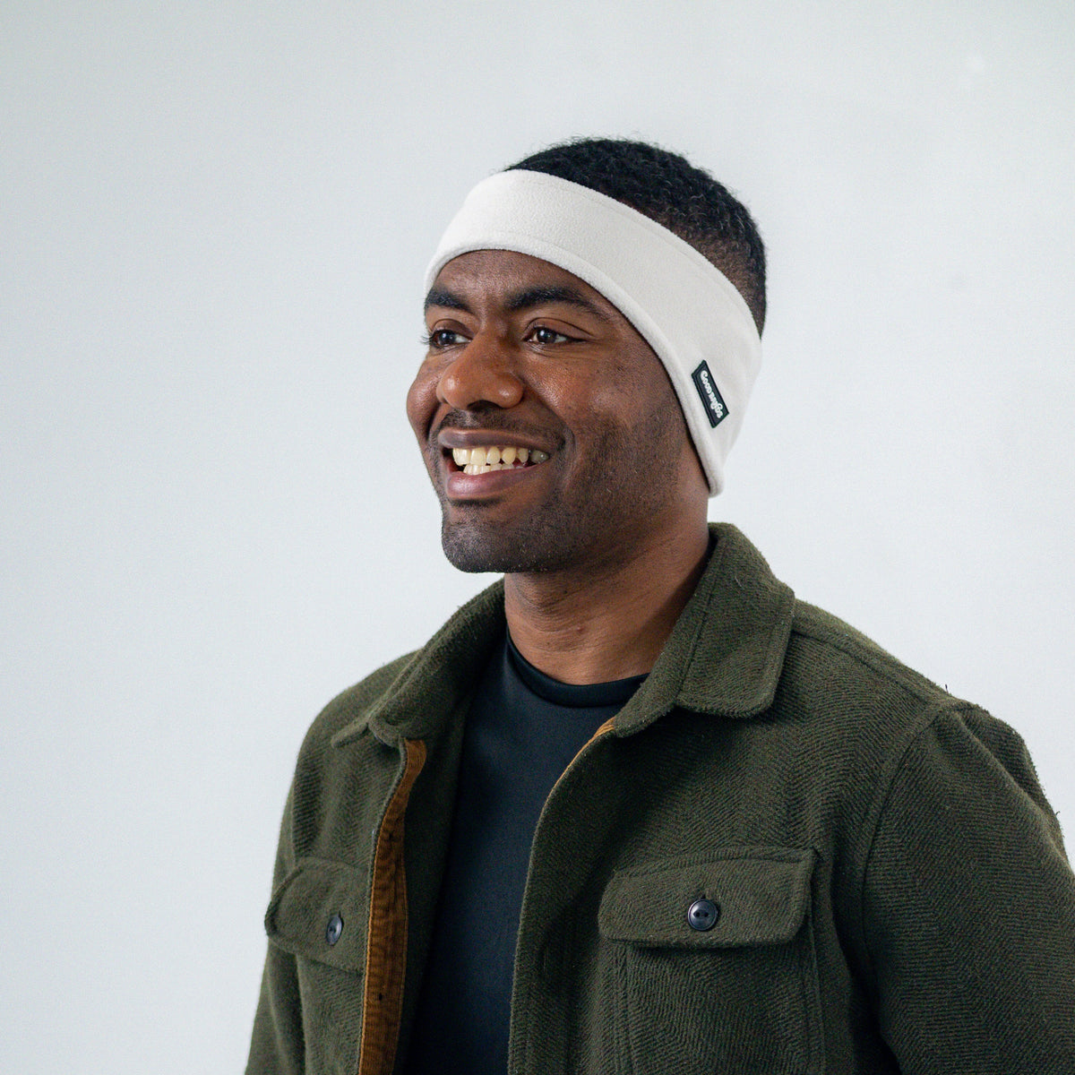 Man wearing a cream white Good Bands winter ear warmer with an olive fleece jacket against a light gray studio background